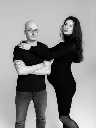 Pregnant brunette girl in a black dress with a throat and a man in a T-shirt and jeans on a gray...