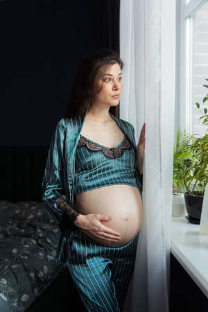 Attractive pregnant woman in pajamas sits in bed and holds her belly. Last months of pregnancy.の写真素材