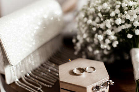 Wedding rings lie on a wooden box next to the bride's bouquetの写真素材