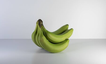 Green raw bananas on the grey and clean table with naturel lights and shadows. Healty fruits, vegan and diet nutritions.の写真素材