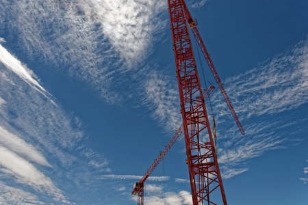 Tower crane painted red against the blue sky filled with clouds