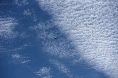 Airplane flying at a height against a brilliant blue sky filled with cloudsの写真素材