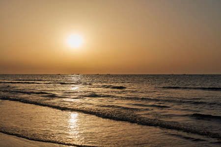 Beautiful golden sunset with the sun reflecting on the water and a row of fishing boats on the...