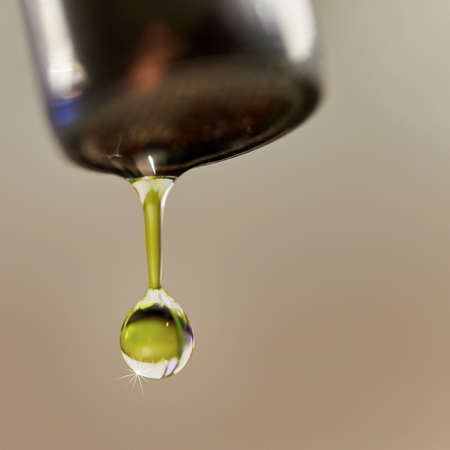A drop of water hanging from a faucet with a green tinge from the background and a sparkle on its highlightの写真素材