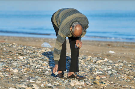 An elderly person stooping to pick up a shell on a beach