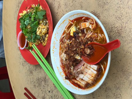 Rice noodle soup with pork in white bowl and oyster omelette in red plate on wooden tableの写真素材