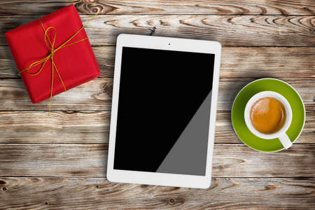 Gift box, cup of coffee and digital tablet on wooden background