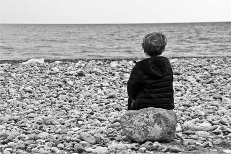 child sitting on a rock on the beach in winterの写真素材
