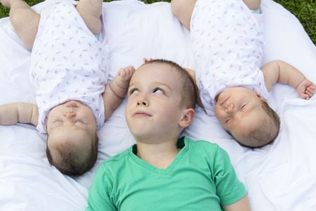 brother looking at twin sister lying in the parkの写真素材