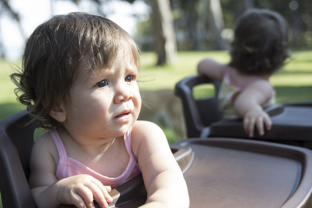 twin baby sitting in feeding chair
