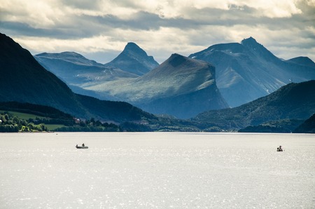 Magical view of two boats sailing on a Norwegian fjord with mountains behind and cloudy skyの写真素材