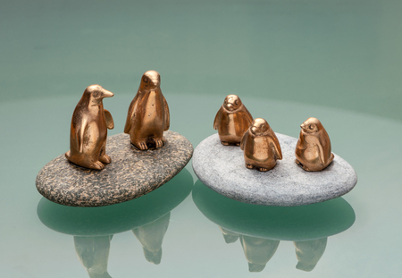 Bronze figurines of five penguins standing on polished stones reflective surfaceの写真素材
