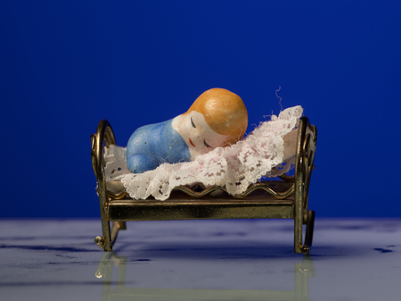 Closeup of a small figurine of a child sleeping in bed, blue backgroundの写真素材