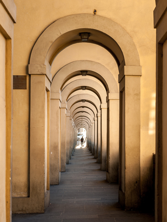 Passageway in Florence (Italy) with round arches and person at the endの写真素材