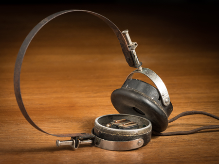 Closeup of old broken vintage ear phones on a brown wooden tableの写真素材