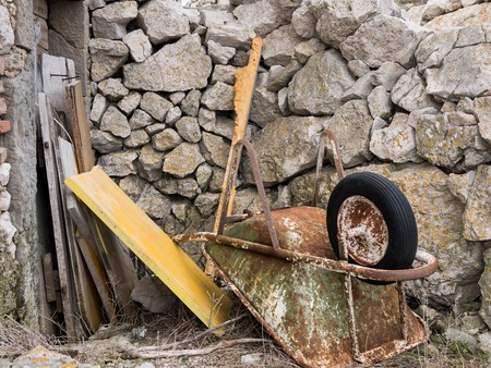 Old rusty wheelbarrow lying on the floor in front of stone wall in Lubenice, Cres Croatiaの写真素材