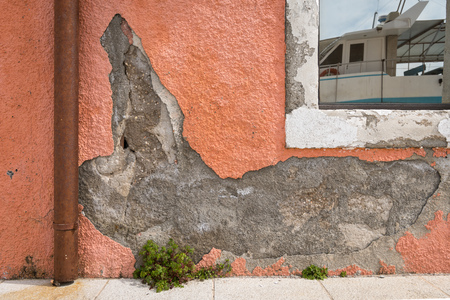 Crumbled plaster of an orange wall, reflection of a boat in the window, harbour in Cres (Croatia)の写真素材