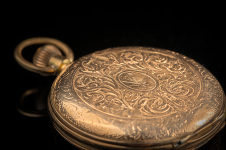 Closeup of an old, used golden pocket watch on a black reflective surface, closed lidの写真素材