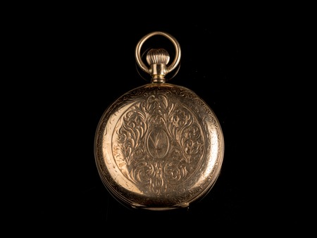 Closeup of an old, used golden pocket watch on a black reflective surface, closed lidの写真素材
