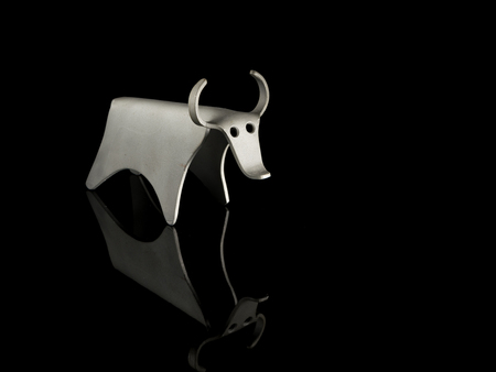 Abstract figurine of a bull made of bent aluminium sheet, standing on a black reflective surfaceの写真素材