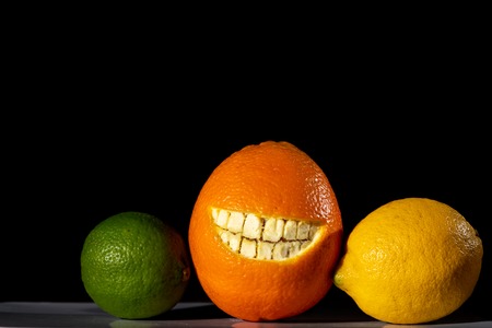 Orange with a cut smile in the skin, lemon and lime, black backgroundの写真素材