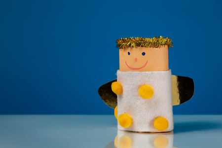 A small figure of an angel made of a toilet paper roll by a child on blue backgroundの写真素材
