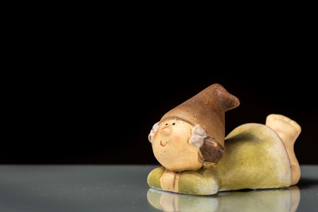 A small figurine of a gnome lying on a reflective surface isolated on black backgroundの写真素材