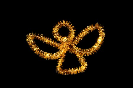 Abstract figure of an angel used for decorating a christmas tree and golden on black backgroundの写真素材