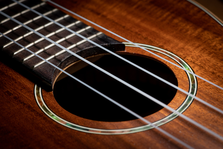 Closeup of a small brown ukulele guitar with strings