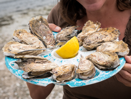 Closeup of a girl holding a plate with oysters and a lemon (Normandy, France)の写真素材