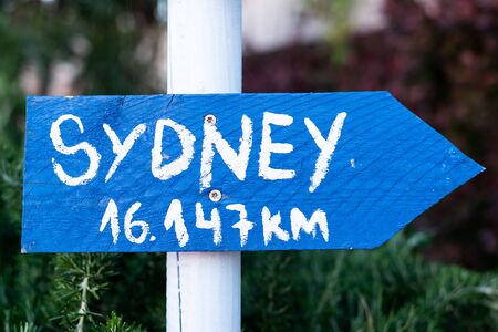 blue sign with white font on a white pole which points to Sydneyの写真素材