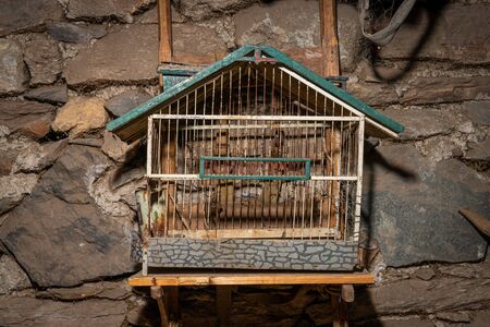 Closeup of an old birdcage hanging in front of a stone wallの写真素材