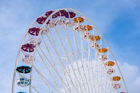 Upper part of ferris wheel with different colored gondolas, blue sky