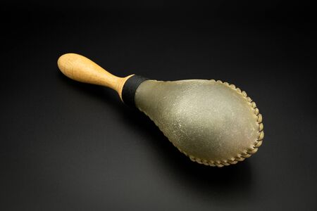 Closeup of a rawhide maracas lying on a black underground