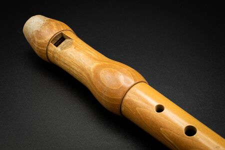 Closeup of a wooden soprano recorder lying on black background