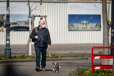 Vienna, Austria - April 04, 2020: Man with dog wearing a mask on the street, protection against corona virus infection, sunny day in springtimeのeditorial素材