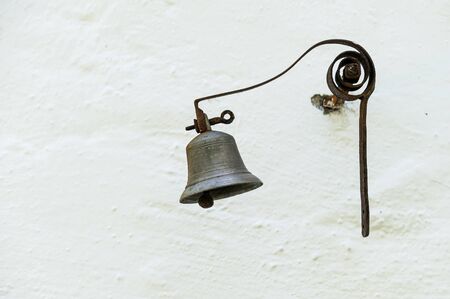 Closeup of an old small bell made of bronze hanging on a white wallの写真素材