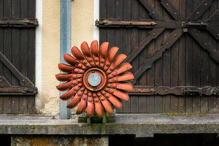 An old orange Pelton wheel hanging outside, cloudy day in the Austrian Alps