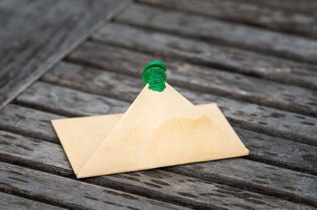 Open brown paper envelope lying on a wooden table outdoors, green seal