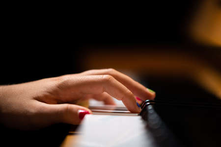 Hand of a girl with colored finger nails playing the piano