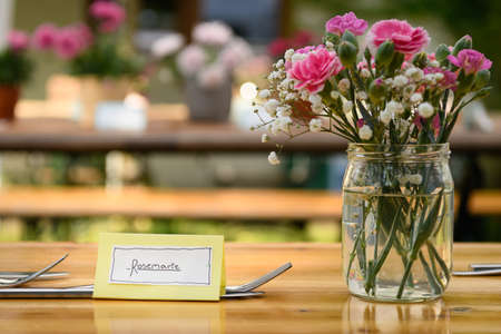 Hand written table name card and cutlery on a wooden table, flowers in the background, wedding, outdoorsの写真素材