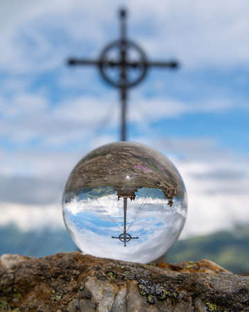 Glass sphere lying on a rock in front of summit cross, Ederplan, cloudy day in summer, alps in East Tyrol (Austria)の写真素材