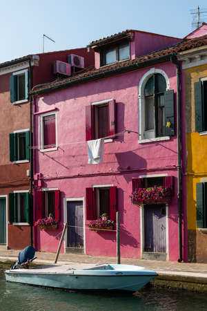 Burano, Italy - October 29, 2021: Colorful houses of Burano on a sunny day in autumn, clear sky, laundry hung out for drying, canal with boatのeditorial素材