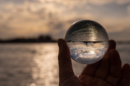Hand holding glass sphere in front of sunset in Venice (Italy), reflection in sea