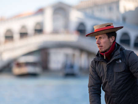 Venice, Italy - October 29, 2021: Portrait of a gondolier steering a gondola on canale grande, Ponte Rialto in background, sunny day in winterのeditorial素材