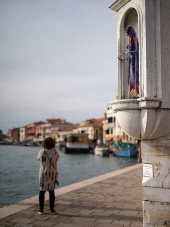 Murano, Italy - October 25, 2021: Statue of holy Mary made of colorful glass, house corner, cloudy day in autumnのeditorial素材