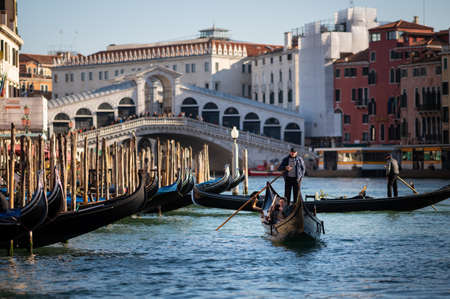 Venice, Italy - October 29, 2021: A gondolier steering a gondola on canale grande, Ponte Rialto in background, sunny day in winterのeditorial素材