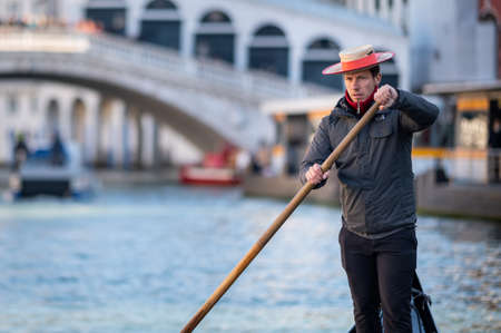 Venice, Italy - October 29, 2021: Portrait of a gondolier steering a gondola on canale grande, Ponte Rialto in background, sunny day in winterのeditorial素材