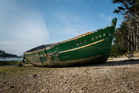 Lanilis, France - August 10, 2020: Old green boat lying on the beach, low tide, sunny day in summerのeditorial素材