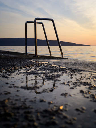 Ladder into the sea at the beach in Cres (Croatia), sunset in springtime, reflections in puddleの写真素材